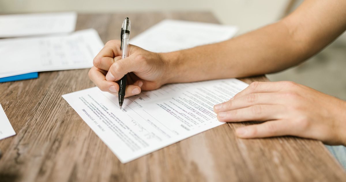 Hand filling out a printed form with a black pen
